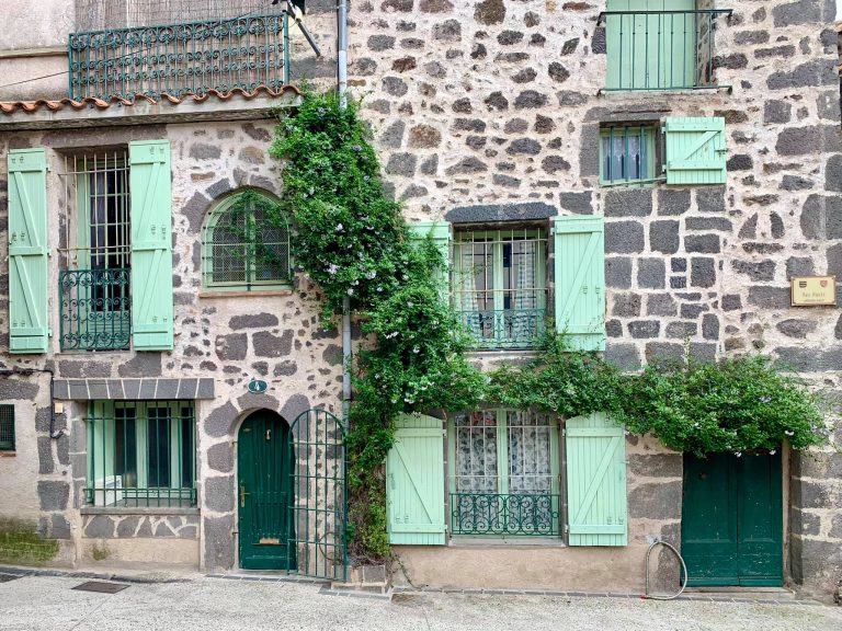 building in france with grey bricks and turquoise green shuttes and folliage